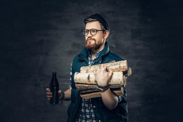 Een dronken, bebaarde man gekleed in een fleece-shirt houdt brandhout en ambachtelijk flesjes bier vast.