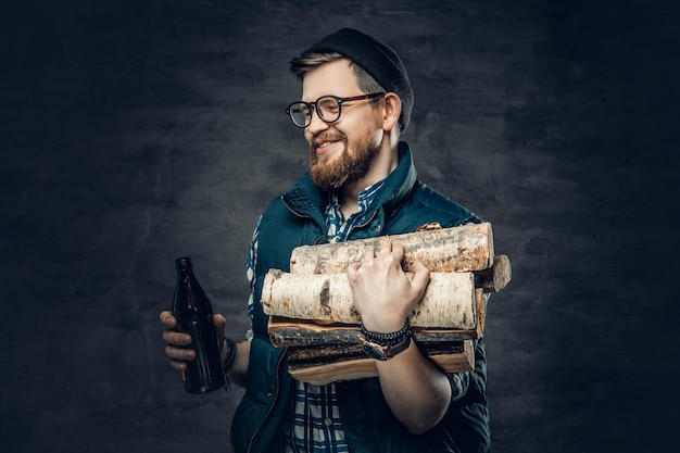 Een dronken, bebaarde man gekleed in een fleece-shirt houdt brandhout en ambachtelijk flesjes bier vast.