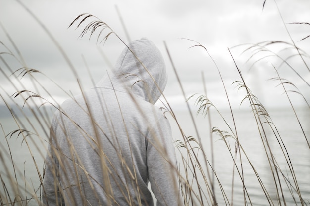 Een eenzame, droevige persoon van achteren met een hoodie die aan zee zit en aan het leven denkt