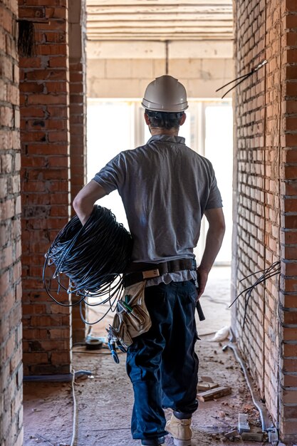 Een elektricien onderzoekt een constructietekening terwijl hij een elektriciteitskabel in zijn hand houdt op een werkplek work