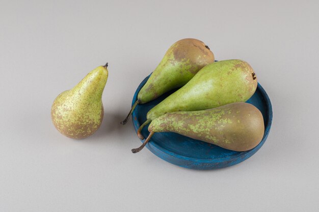 Een enkele peer naast een bundel peren op een schaal op marmer