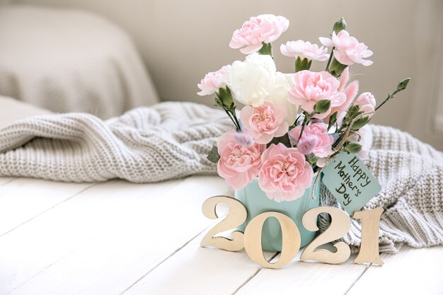 Een feestelijke compositie met verse bloemen in een vaas, het jaartal 2021 en een wens voor een gelukkige moederdag op een ansichtkaart.