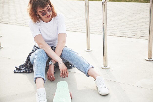 Een foto van een mooi meisje met mooi haar houdt een skateboard op een lang bord en lacht, stadsleven.