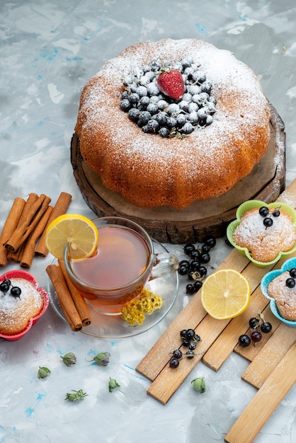 Een fruitcake van bovenaanzicht, heerlijk en rond gevormd met vers blauw, bessen en samen met een kopje thee op een lichte cake