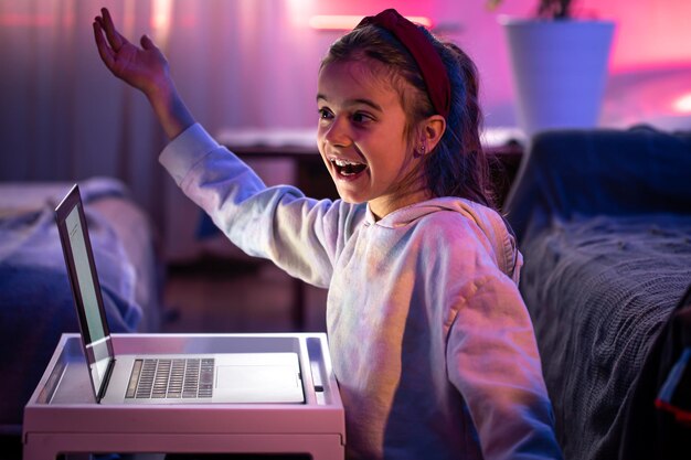 Een gelukkig klein meisje gebruikt 's avonds laat een laptop