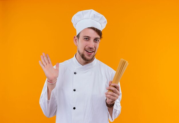 Een gelukkige jonge bebaarde chef-kokmens in witte uniforme spaghetti houden op een oranje muur