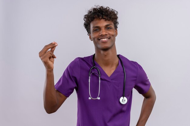 Een gelukkige jonge knappe donkere arts met krullend haar die violet uniform draagt met een stethoscoop die een fillip geeft