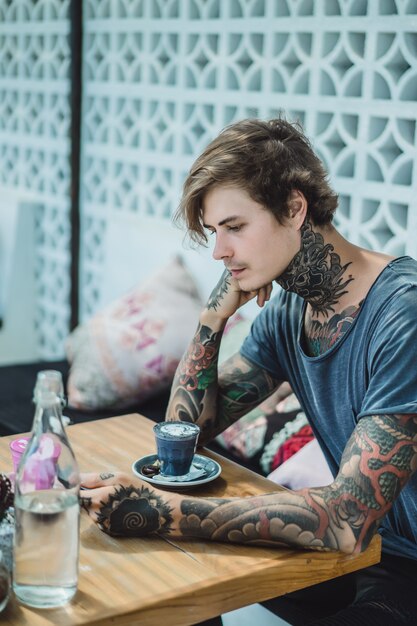 een getatoeëerde man drinkt een kleurrijke koffie in een café.