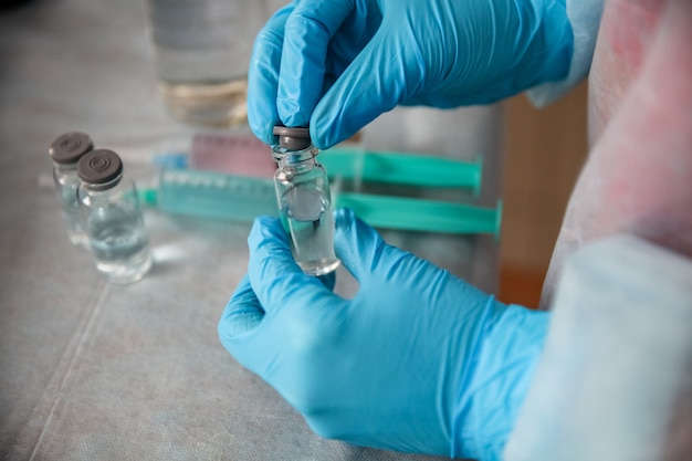 Een gezondheidswerker die in blauwe handschoenen een vaccinflesje boven de medische lijst houdt