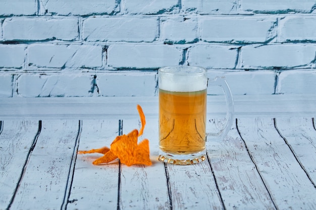 Een glas bier en chips op een blauwe tafel.