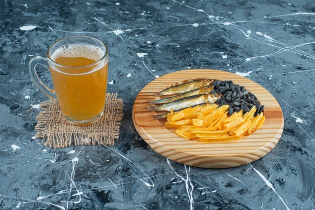 Een glas bier op textuur en hapjes op houten plaat, op de blauwe achtergrond.