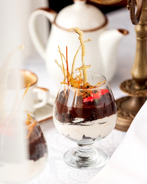 Een glas chocoladedessert met vanillecrème gegarneerd met karameldecoratie en bloem