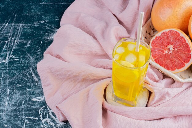 Een glas limonade met schijfjes citroen en grapefruits op marmeren oppervlak.