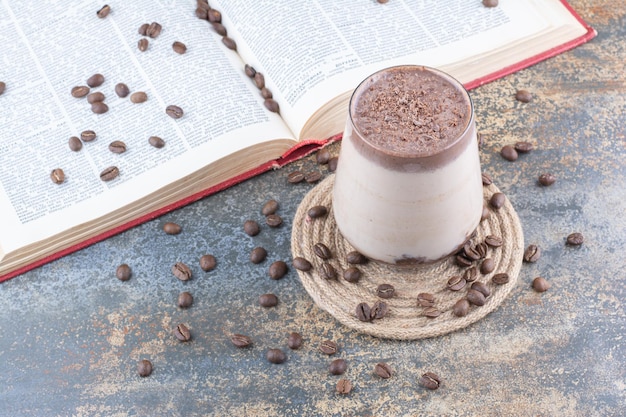 Gratis foto een glas melk met geopend boek en koffiebonen op marmeren achtergrond. hoge kwaliteit foto