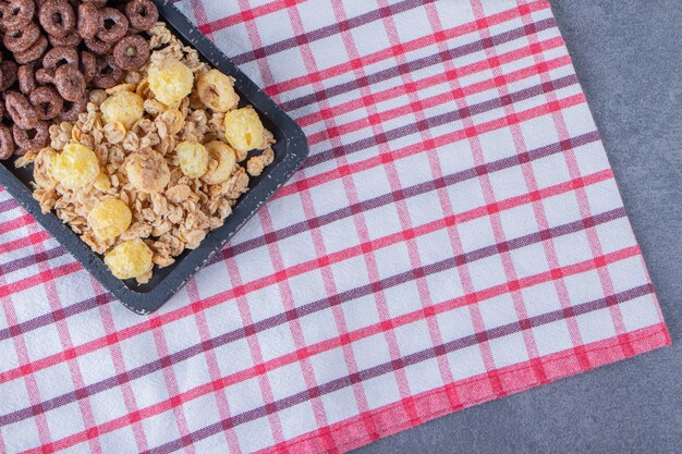 Een glas melk naast maïsringen en cornflakes in een bord op theedoek, op de marmeren tafel.