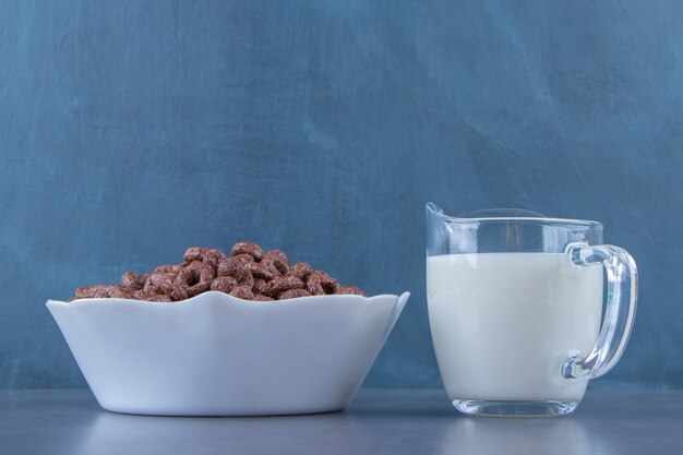 Een glas melk naast maïsringen in een kom, op de marmeren achtergrond.