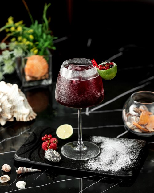 Een glas rode cocktail gegarneerd met limoenschil en veenbessen