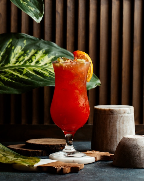 Een glas rode cocktail met ijs en een sinaasappelplak