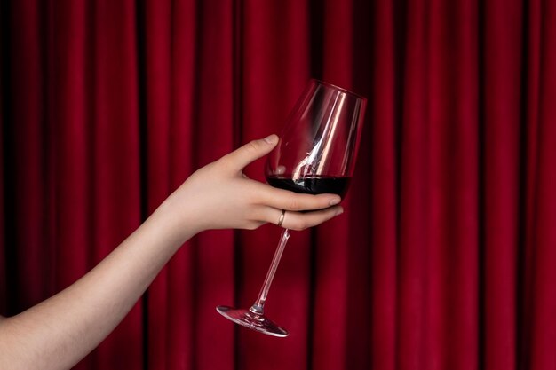 Een glas rode wijn in een vrouwelijke hand op een rode textuurachtergrond
