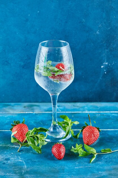 Een glas sap met aardbeien en munt binnen op blauwe ondergrond