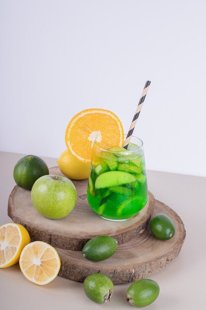 Een glas sap met fruitplakken en vers fruit op witte muur.