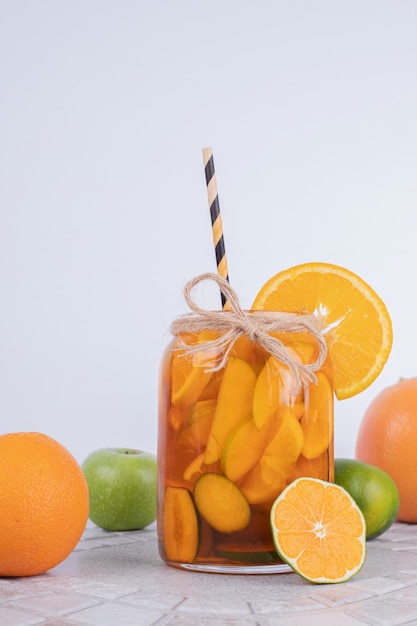 Een glas sap met fruitplakken en vers fruit op witte muur.