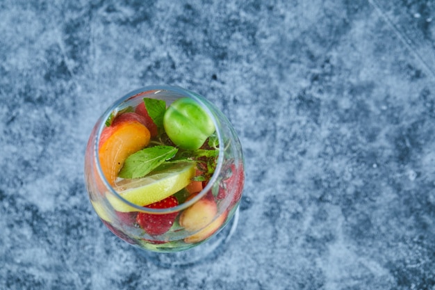 Gratis foto een glas sap met hele vruchten binnen op blauwe ondergrond