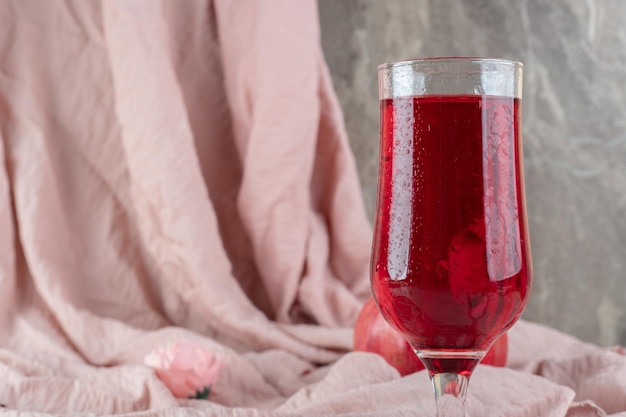 Een glas sap met verse granaatappel op roze doek