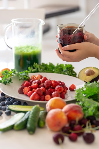 Een glas smoothie van bessen in de hand van een kind thuis in de keuken