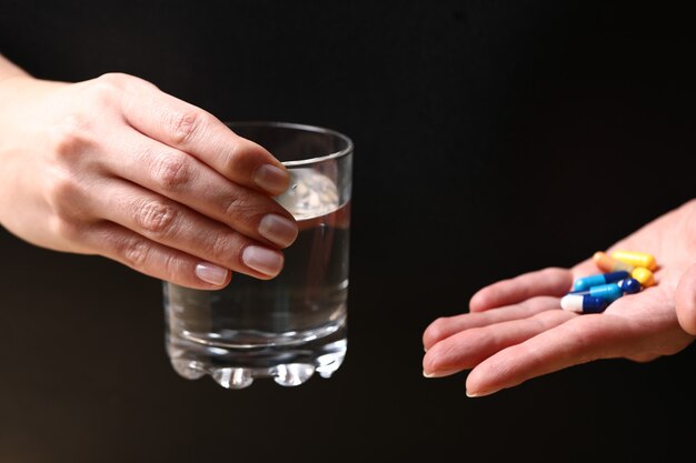 Een glas water en medische pillen in handen van een persoon