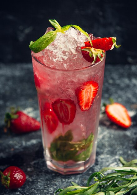 een glas water met plakjes aardbeien, muntblaadjes en ijs