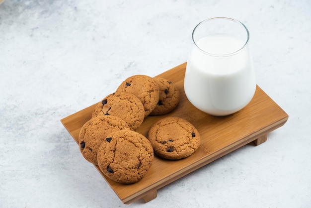 Een glazen beker met chocoladekoekjes op een houten bureau.