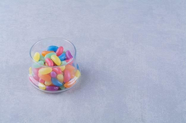Een glazen beker vol kleurrijke bonensnoepjes op een grijze achtergrond. Foto van hoge kwaliteit
