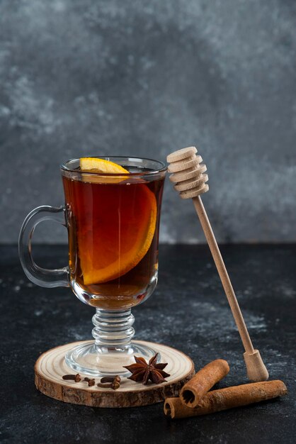 Een glazen kopje thee en met kaneelstokjes en houten lepel.