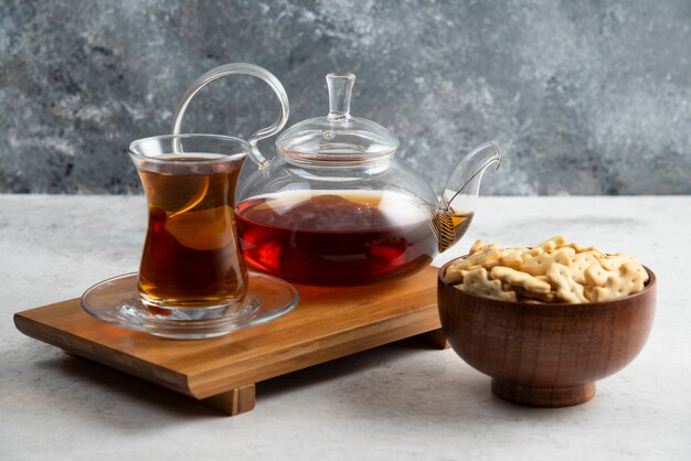 Een glazen kopje thee met een houten kom vol crackers.