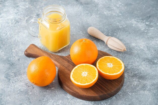Een glazen kruik sap met vers oranje fruit op stenen tafel.