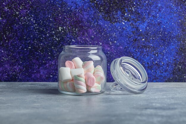 Een glazen pot met heerlijke marshmallows op een grijze achtergrond.