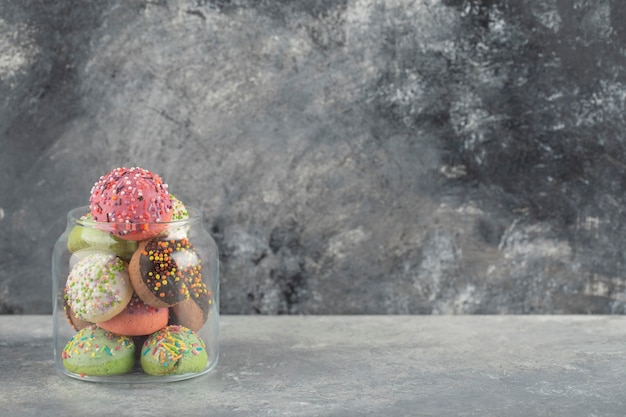 Een glazen pot vol kleine kleurrijke donuts.