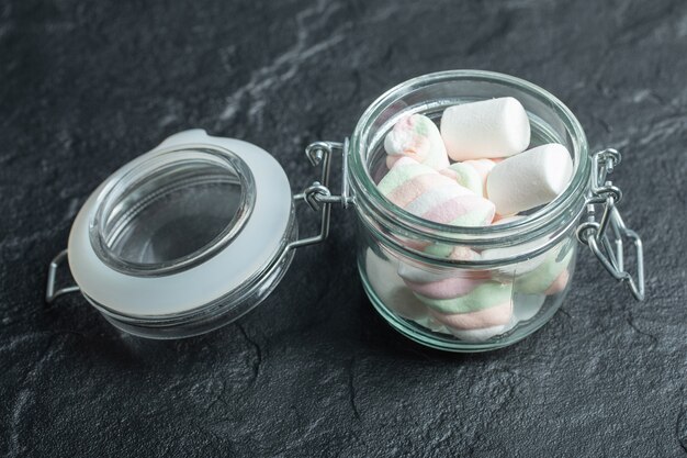 Een glazen pot vol marshmallows op een donkere ondergrond.