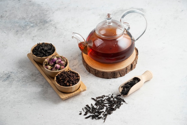 Een glazen theepot met houten schaaltjes losse thee.