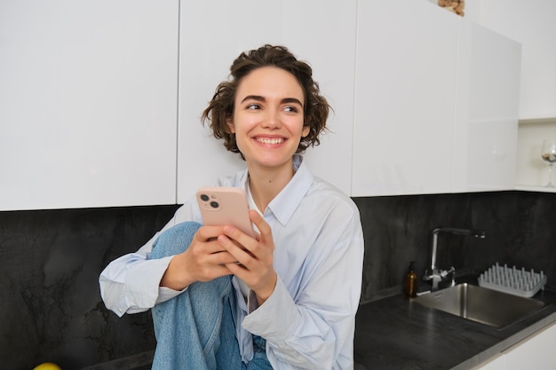Gratis foto een glimlachend donkerbruin meisje dat thuis met een smartphone zit, bestelt afhaalmaaltijden via de mobiele telefoonapp