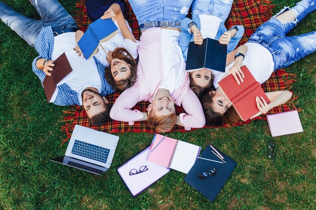 Een groep jonge mooie mensen ligt op het gras. Studenten ontspannen na de lessen op de campus