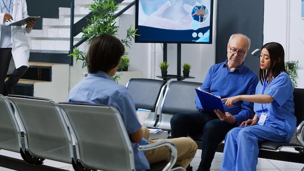 Een groep mensen in een vergadering met een monitor die een blauwe labjas en een man in een blauwe scrub toont.