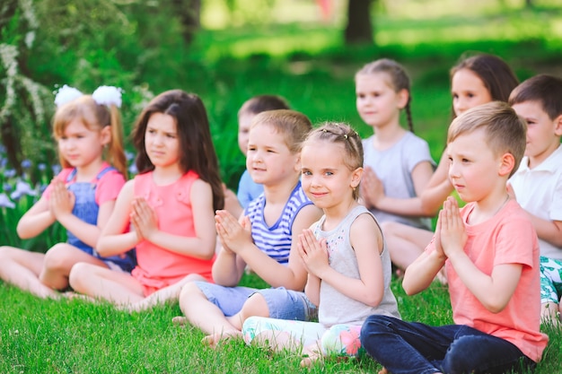 Een grote groep kinderen die zich bezighouden met yoga in het park zittend op het gras.