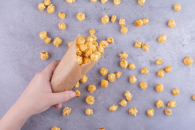 Een hand die een pakje met karamel gecoate popcorn op marmeren achtergrond morst. Hoge kwaliteit foto