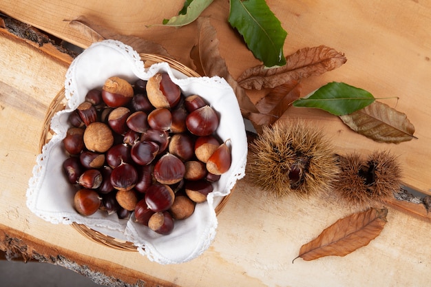 Een handvol seizoenskastanjes en hun egel op een houten plank met schors, met herfstbladeren