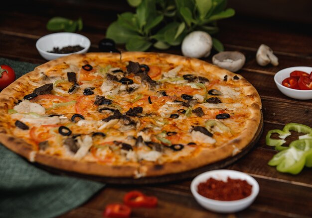 Een hele gemengde olijfpizza geserveerd op een houten bord met kruiden.