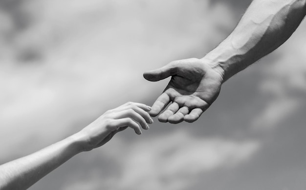 Een helpende hand bieden. handen van man en vrouw op blauwe hemelachtergrond. een helpende hand bieden. solidariteit, mededogen en liefdadigheid, redding. zwart en wit.