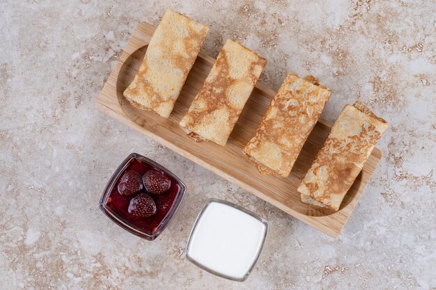 Een houten bord met lekkere pannenkoeken en aardbeienjam