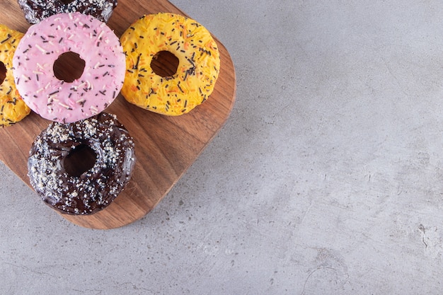 Een houten bord van donuts met chocolade en gele coating